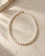Pearl necklace arranged on warm limestone in soft daylight.