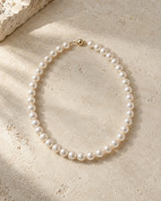 Pearl necklace arranged on warm limestone in soft daylight.