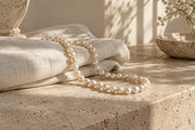 Pearl jewelry arranged with textured ivory fabric and natural objects.