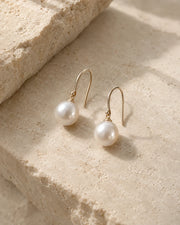 Pair of pearl earrings on a warm ivory background.