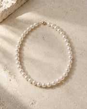 Pearl necklace arranged on warm limestone in soft daylight.