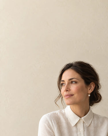 Woman in an ivory shirt wearing a pearl drop earring with a softly lit ivory background.