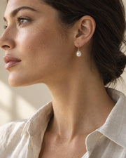 Woman wearing pearl earrings with a neutral outfit in soft daylight.